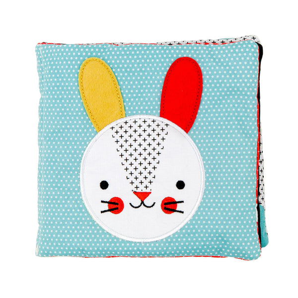 The Organic Soft Book & Teether Set by Petit Collage features a soft fabric baby book with a blue polka dot cover and an embroidered rabbit face with one yellow and one red ear.