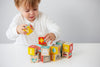 A young child builds with Petit Collage ABC Wooden Alphabet Blocks, stacking colorful wooden letters and animal blocks on a white table.