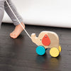 A child pulls the Petit Collage Wooden Jumbo Jumping Elephant Pull Toy with colorful wheels across a dark floor.