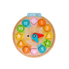 The Petit Collage Multi-Language + Counting + Colors Wooden Learning Clock features colorful numbered hour shapes, blue and red movable hands, and a cat face at the center, set to 5:15.