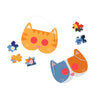 Two cat-shaped masks (one orange, one blue-and-white) from Petit Collage’s Catventures - The Sleepover: 100-Piece Decoder Puzzle are placed next to four colorful puzzle pieces on a white background.