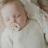A baby with a pacifier sleeps peacefully, dressed in the Petit Collage Little Monkey Baby Gift Set and lying on a patterned blanket.