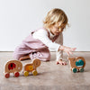 A young child plays on the floor with the Petit Collage Wooden Push Along Elephant Toy.