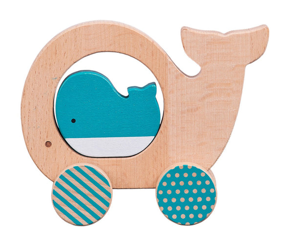 The Petit Collage Wooden Push Along Whale Toy features a whale-shaped wooden design with two decorated wheels and a small blue whale figure inside.