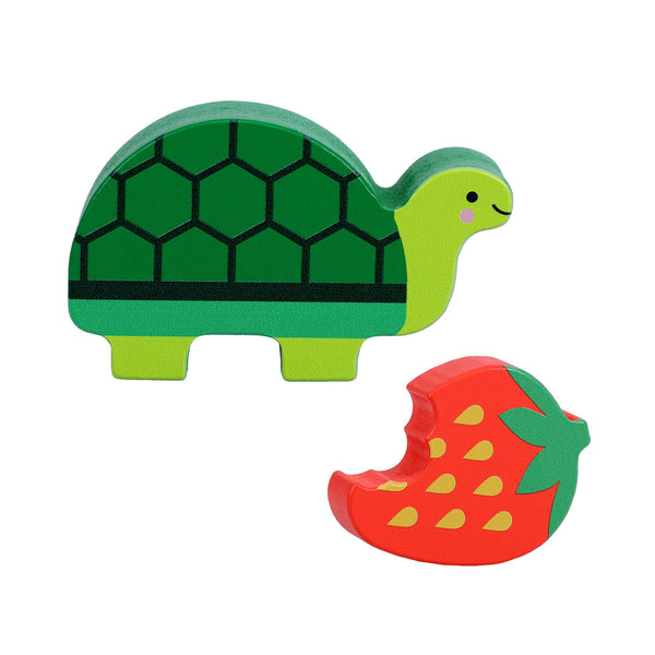 A Petit Collage Petit Pals: Tilly Tortoise figurine in green and a red wooden bitten strawberry, both on a white background.