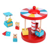 The Petit Collage Merry-Go-Round Wooden Carousel features bright red, blue, yellow, and white colors, animal figures, a ticket booth with tickets, and three carousel seats.