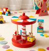 The Petit Collage Merry-Go-Round Wooden Carousel with animal figures sits on a light, multicolored-dot carpet, while other wooden toys like a ferris wheel and cars are visible in the background.