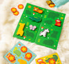 The Petit Collage First Bingo Game: Animal Friends features wooden animal-shaped pieces like giraffe, zebra, and elephant on a soft white surface, with extra yellow cards and star-shaped pieces alongside.