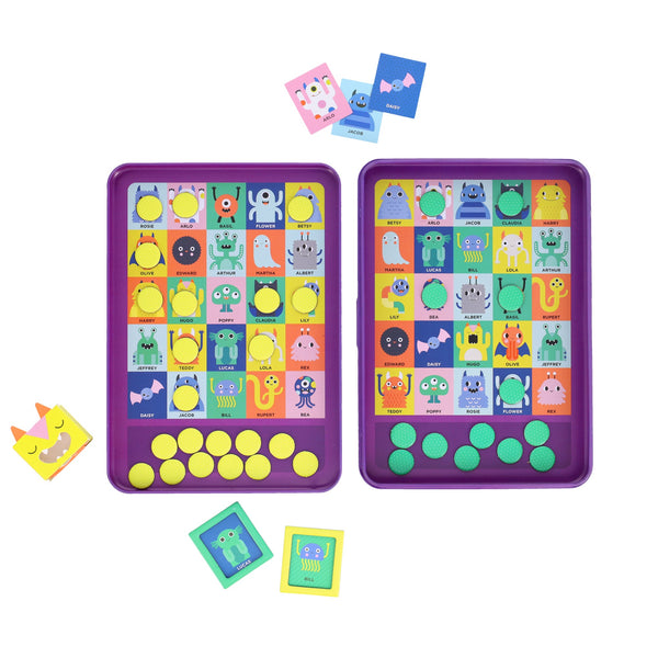 The Petit Collage Whos That Monster? Magnetic Travel Game features two purple boards with colorful cartoon monsters, yellow circular tokens, and monster-themed cards arranged around the boards.