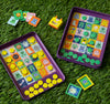 The Petit Collage Whos That Monster? Magnetic Travel Game features two colorful monster-themed bingo boards, yellow and green markers, matching monster cards, and a small yellow box with a cartoon face.