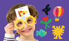 A smiling child wearing oversized yellow glasses plays Guessing Things: A What Am I? Game by Petit Collage, holding a card with a pizza picture on their forehead. Colorful drawings are set against a purple background.