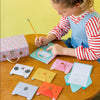 A child writes in a notebook at a table with Petit Collage’s Animal Pals My Stationery Set, featuring colorful animal-shaped cards, a polka dot box, and a closed pencil.