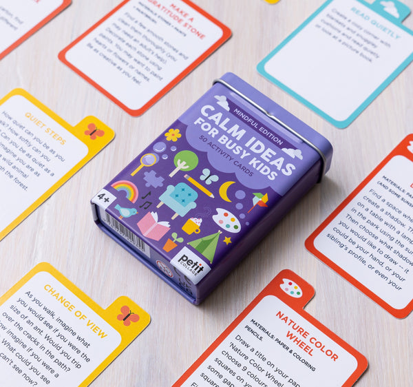 A box labeled Calm Ideas for Busy Kids: Mindful Edition by Petit Collage rests on a table, surrounded by colorful activity cards featuring instructions and illustrations.