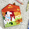 The Petit Collage Coloring Book with Stickers: Pets rests on a light carpet with crayons nearby. The cover shows a dog, cat, rabbit, turtle, and bird.