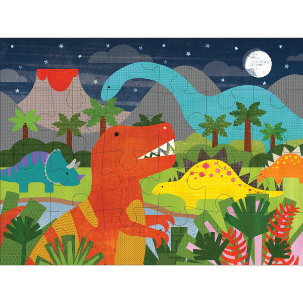 The Petit Collage Dinosaur Kingdom 24-Piece Floor Puzzle features colorful dinosaurs in a prehistoric jungle at night, with a full moon, stars, volcano, trees, and lush plants in the background.