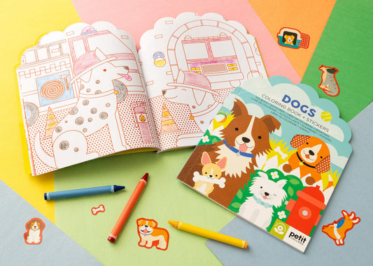 The Petit Collage Dogs Coloring Book + Stickers set is shown open with crayons and loose dog stickers on a colorful background.