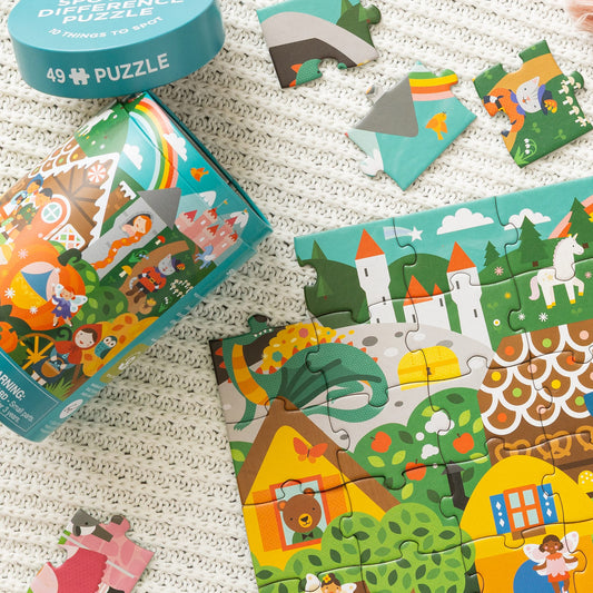 The Petit Collage "Spot the Difference Puzzle: Fairy Tales" is a vibrant 49-piece puzzle featuring fantasy illustrations, shown partially assembled on a textured surface with loose pieces and its container nearby.