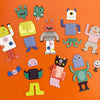 The Petit Collage Mixed Up Monsters Magnetic Play Set features colorful, patterned monster characters arranged on an orange background.