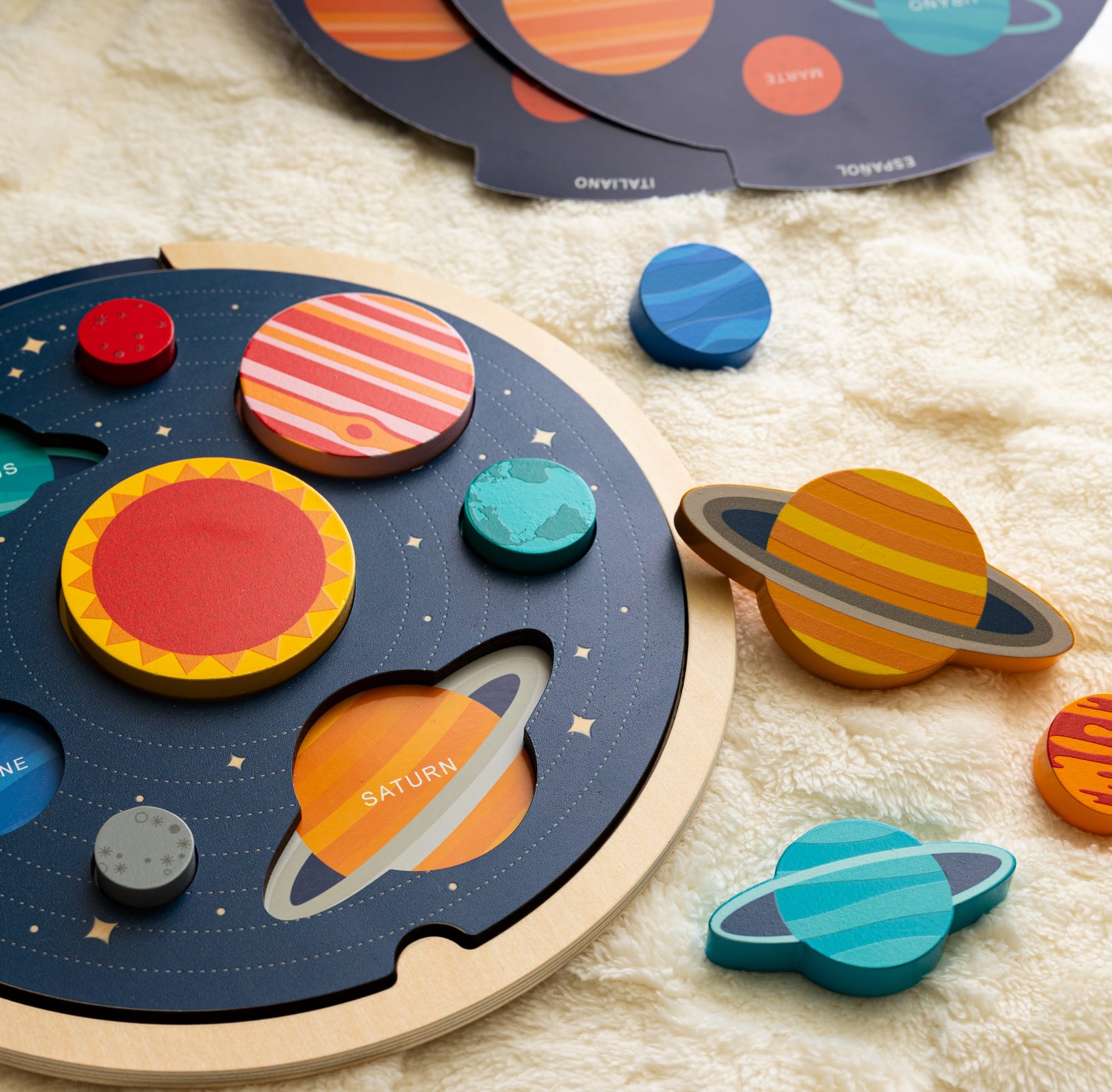 The Petit Collage Multi-Language Solar System Wooden Tray Puzzle features vibrant planet and sun pieces, arranged on a soft beige surface.