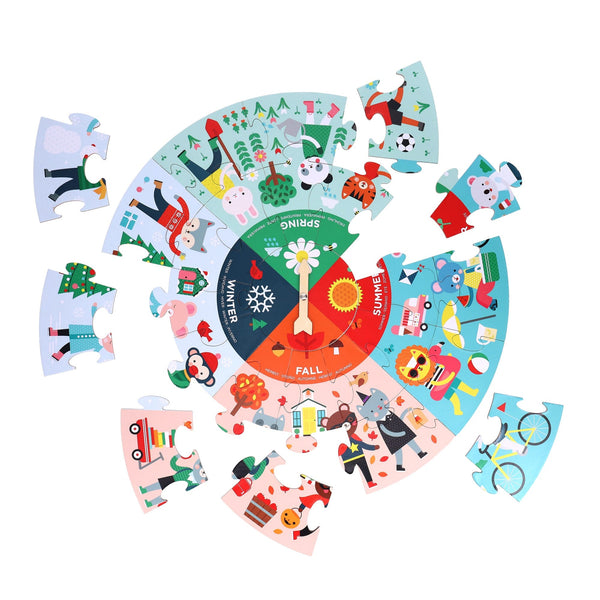 The Petit Collage Seasons 25-Piece Floor Puzzle is a circular jigsaw featuring cartoon scenes of winter, spring, summer, and fall arranged around a central spinner.