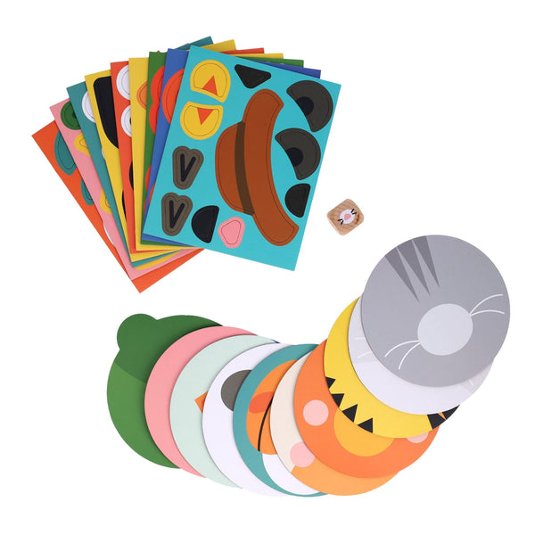 The Make Funny Faces Game by Petit Collage features colorful sheets with animal faces, a small die, and round face cutouts arranged on a white surface.