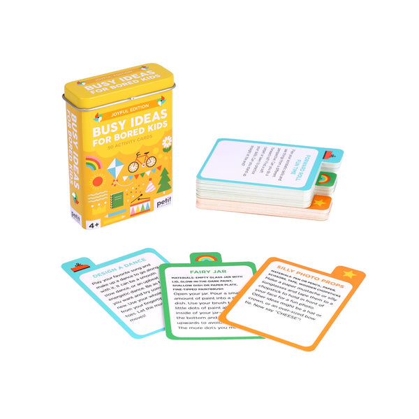 The Busy Ideas for Bored Kids Joyful Edition by Petit Collage is shown next to its yellow storage tin, with several colorful activity cards spread out displaying various fun suggestions.