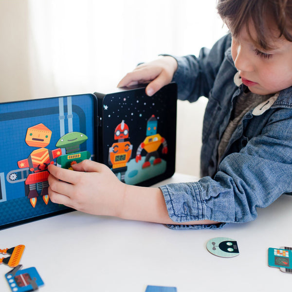 A child uses the Petit Collage Robot Remix Magnetic Play Set to combine robot magnets and create unique robot figures on a magnetic board at a table.