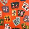 Silly Monkey Card Game by Petit Collage features colorful playing cards with illustrated animals in costumes, spread out on an orange surface.
