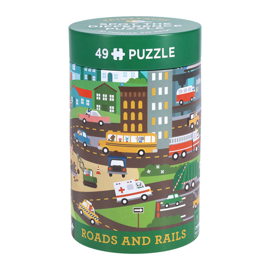 A cylindrical box labeled Spot the Difference Puzzle: Roads and Rails by Petit Collage, featuring colorful illustrations of vehicles, buildings, and roads.