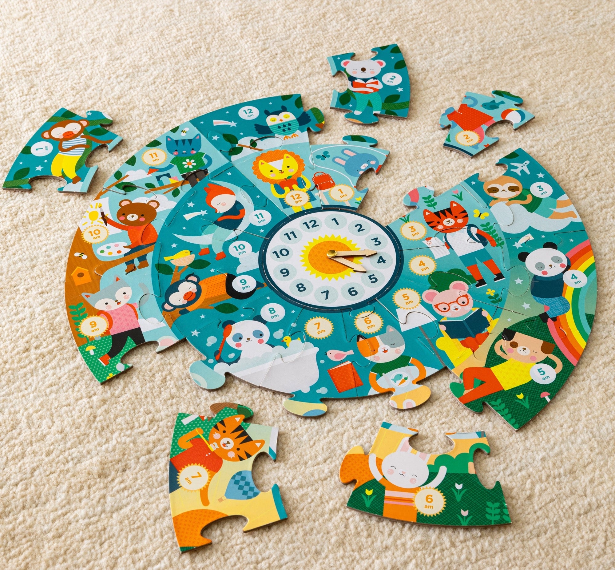 The Petit Collage Telling the Time 25-Piece Floor Puzzle, a colorful animal-themed circular puzzle with a numbered clock at its center, is shown incomplete with several pieces scattered on a beige carpet.
