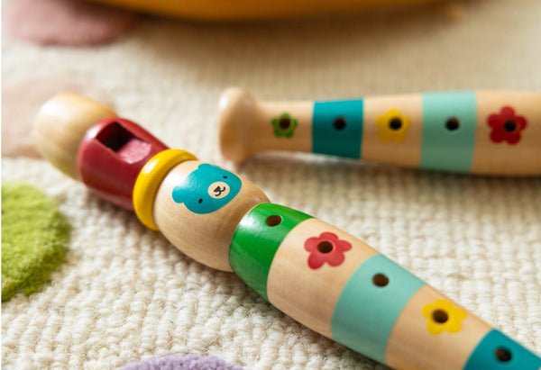 Two Petit Collage Playful Tunes Wooden Recorders with vibrant bear and flower designs are placed on a textured carpet.