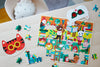 The Petit Collage Busy Readers 100-Piece Decoder Puzzle, featuring colorful animal designs, is partially completed on a table with loose pieces and two animal masks with red glasses nearby.