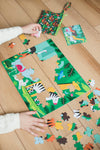 A child assembles the Petit Collage Two Sided Animal Menagerie On-The-Go Puzzle on a wooden floor, with colorful animal pieces and the included small storage bag nearby.