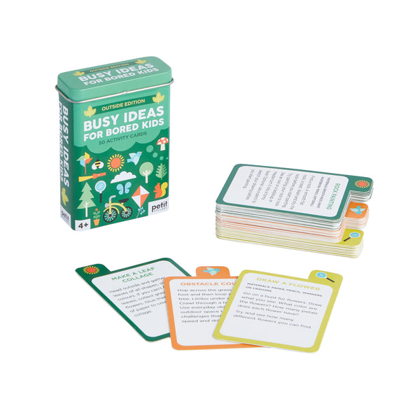 A tin labeled “Busy Ideas for Bored Kids: Outdoor Edition” by Petit Collage sits beside a stack of colorful activity cards, some spread out to reveal various outdoor prompts.