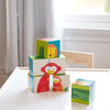 Four vibrant Puzzle Blocks - Wild Animals by Petit Collage, featuring animal illustrations, are stacked on a white table near a sunlit window with sheer curtains.