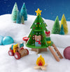 Create a festive scene with the Petit Collage Christmas Treehouse Wooden Play Set, featuring wooden animals, a decorated treehouse, ladder, campfire, toy car, snowy grounds, ornaments, and bottlebrush trees under a starry night.