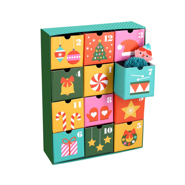The 12 Crafts of Christmas Advent Calendar by Petit Collage features twelve festive drawers with holiday designs. Drawer 7 is open, showing a small gift inside.