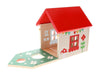The Mouse House Wooden Play Set by Petit Collage features a wooden toy house with a red roof, painted decorative walls, and a green platform with cut-out shapes.