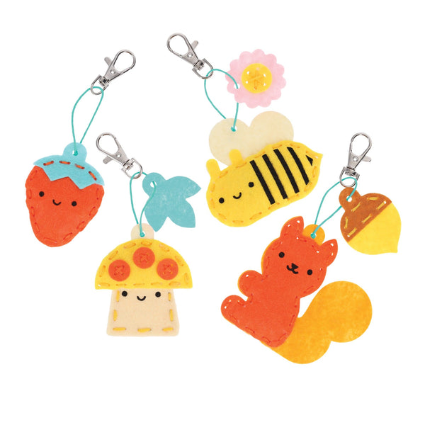 The Petit Collage Mini Craft Kit: Pocket Pal Bag Charms includes four felt keychains—a strawberry, a bee with a flower, a mushroom, and an orange squirrel with an acorn—each with a metal clasp and smiling face.