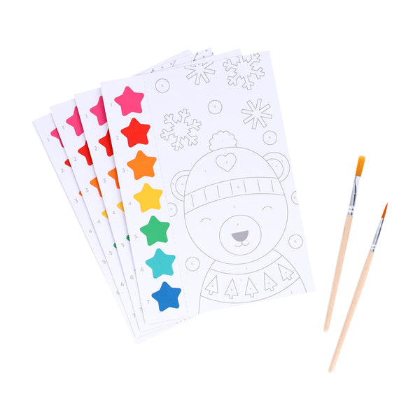 The Petit Collage Paint by Numbers: Christmas set includes five paint-by-number sheets with colorful paint tabs and two brushes, featuring a bear in winter clothing on the top sheet.