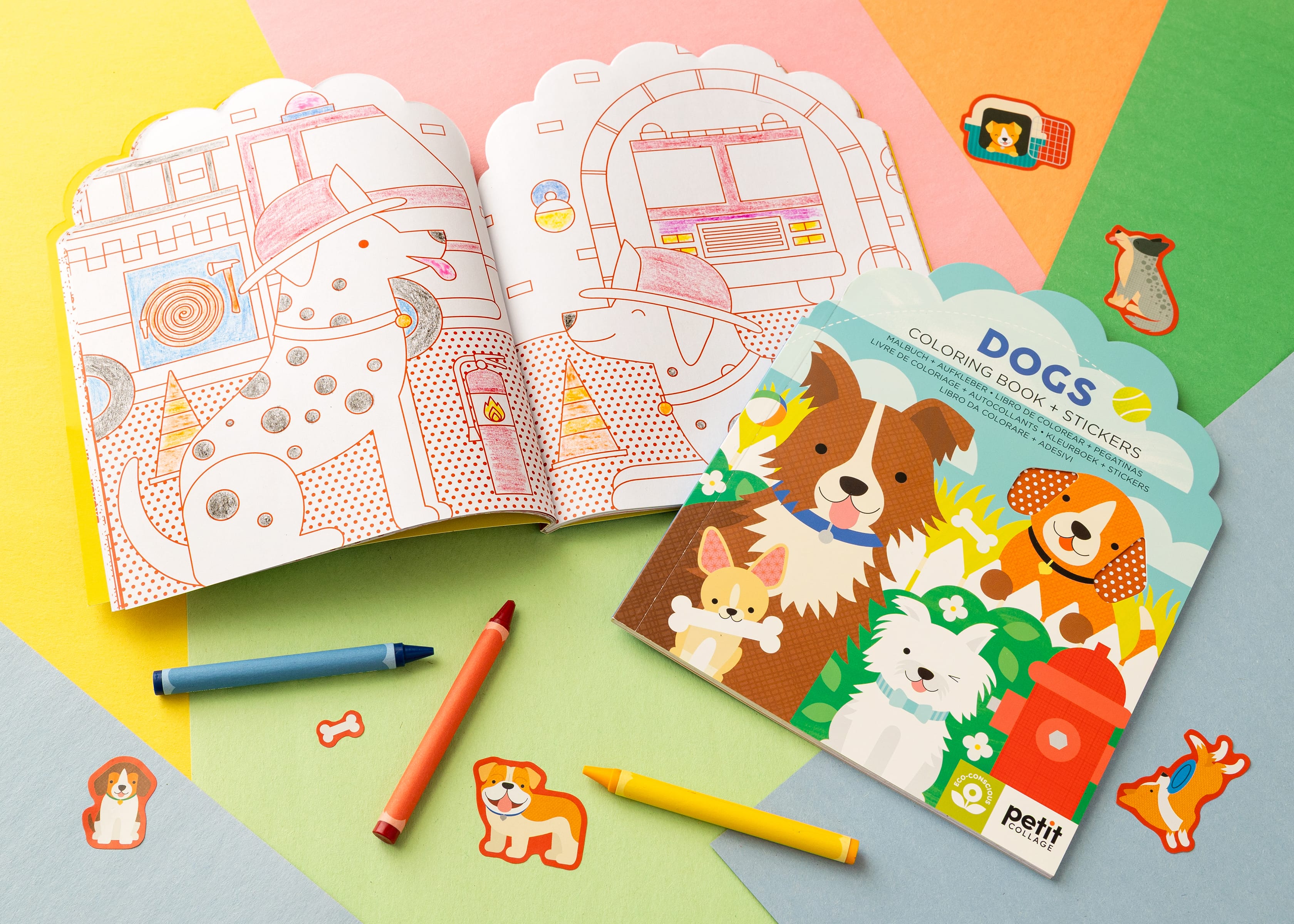 The Petit Collage Dogs Coloring Book + Stickers set is shown open with crayons and loose dog stickers on a colorful background.
