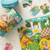 The Petit Collage "Spot the Difference Puzzle: Fairy Tales" is a vibrant 49-piece puzzle featuring fantasy illustrations, shown partially assembled on a textured surface with loose pieces and its container nearby.