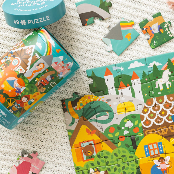 The Petit Collage "Spot the Difference Puzzle: Fairy Tales" is a vibrant 49-piece puzzle featuring fantasy illustrations, shown partially assembled on a textured surface with loose pieces and its container nearby.