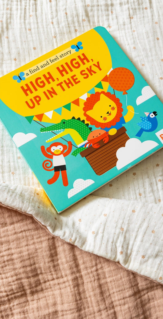 The Petit Collage book A Find and Feel Story: High, High, Up in the Sky features cartoon animals in a hot air balloon, shown on a textured fabric surface.