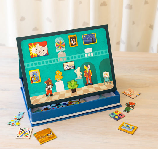The Petit Collage Magnetic Play Scene: My Museum is a children’s board game featuring an illustrated art gallery scene with animal characters and art magnets on a wooden table.
