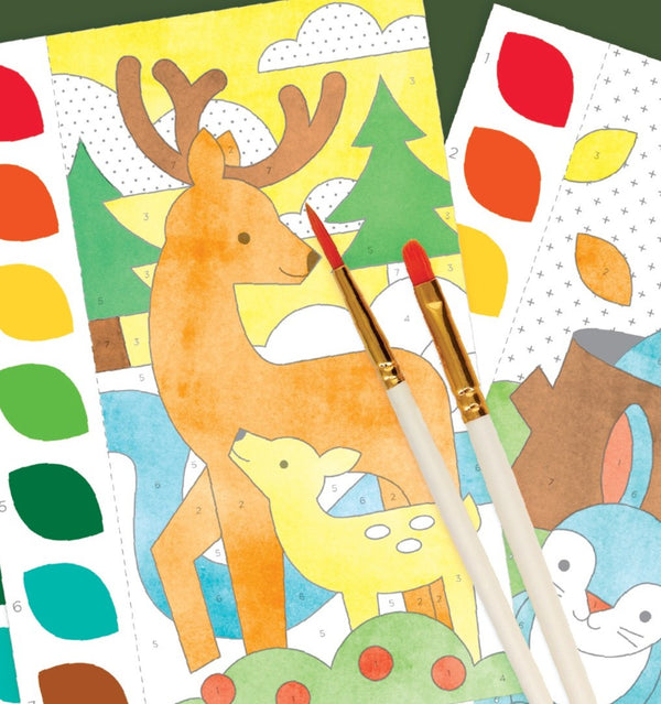 The "Paint by Numbers: Woodland" kit by Petit Collage features a deer and fawn animal scene with paintbrushes, color palettes, and a partially colored rabbit illustration.