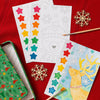 Petit Collage’s Paint by Numbers: Christmas set features watercolors, unfinished and completed holiday animal paintings, paintbrushes, and decorative snowflakes arranged on a red tablecloth.