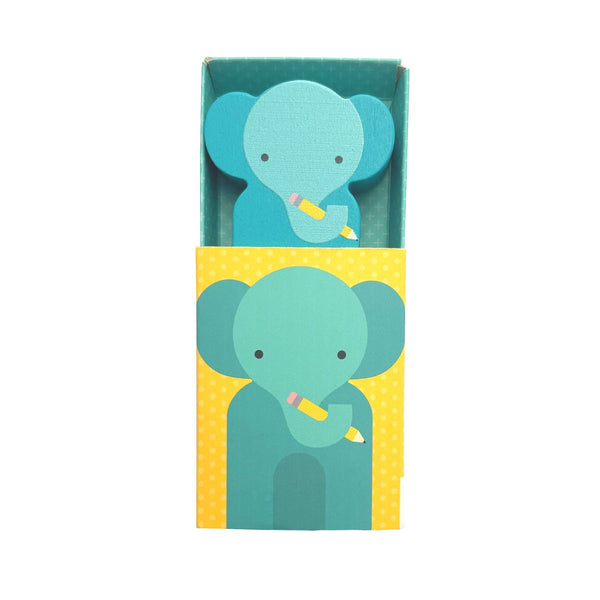 A yellow, white-dotted box from Petit Collage features Eco Ellie— a cartoon blue elephant holding a yellow pencil— perfectly matching the shaped notepad inside. The product is called Wooden Planet Pal: Eco Ellie.